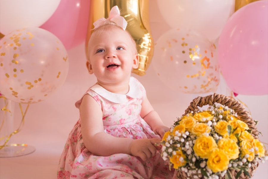 Baby girl in a pink dress sitting on the floor with a basket of flowers