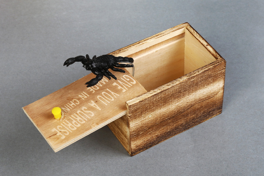 A black plastic scorpion jumping from a wooden box