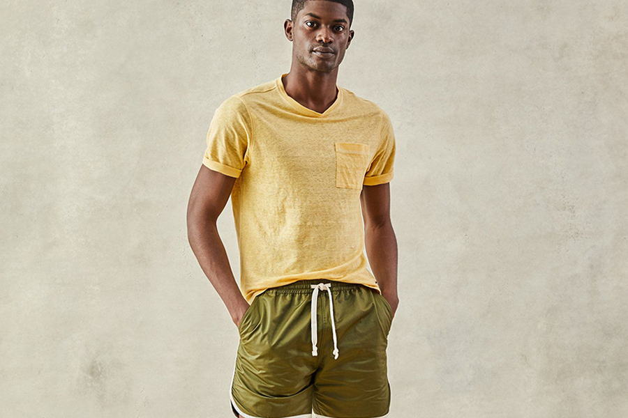 Man standing in yellow tee and olive satin dolphin shorts