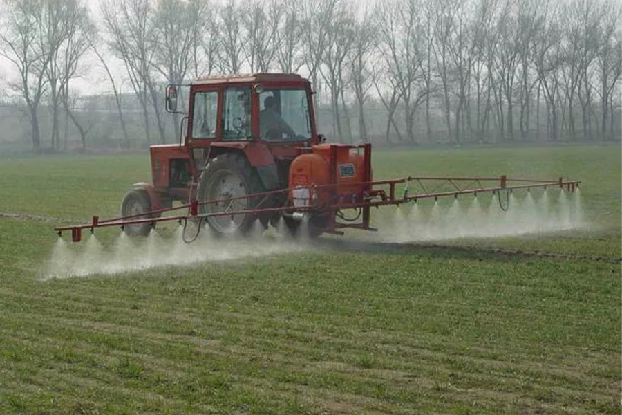 A tractor-mounted boom spraying chemicals over a crop field