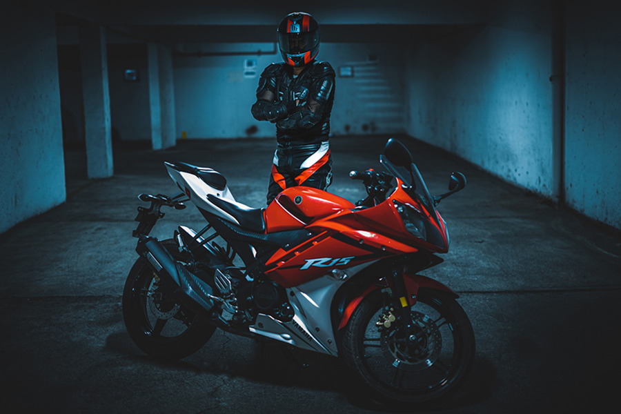 Biker in black body armor standing beside red motorcycle