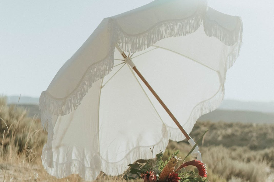 A white tilt button umbrella providing shade for flowers