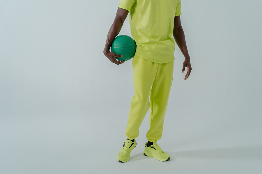 Man in lemon green tee and hybrid joggers holding a ball