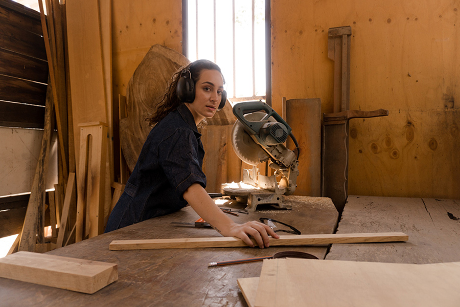 Woman with protective glasses posing with a wood-saw machine