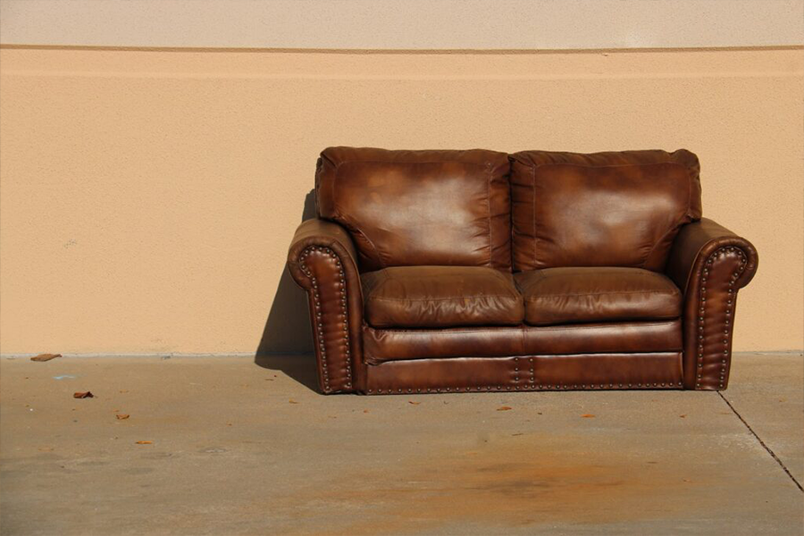 A well-polished brown leather outdoor sofa against a wall