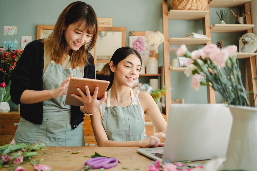 Two multiracial women smiling and working with gadgets