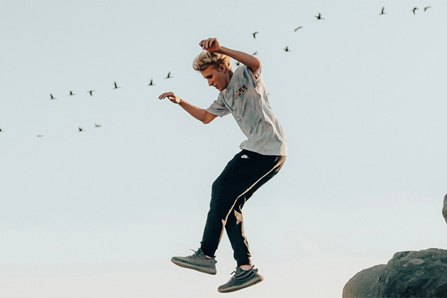 Young man jumping off a cliff in smart joggers