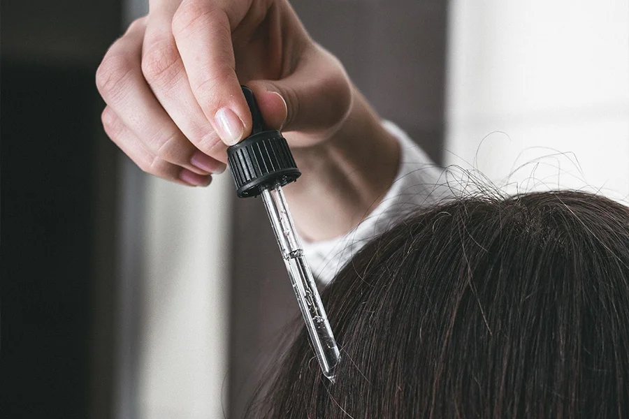 Woman with dark hair applying scalp serum