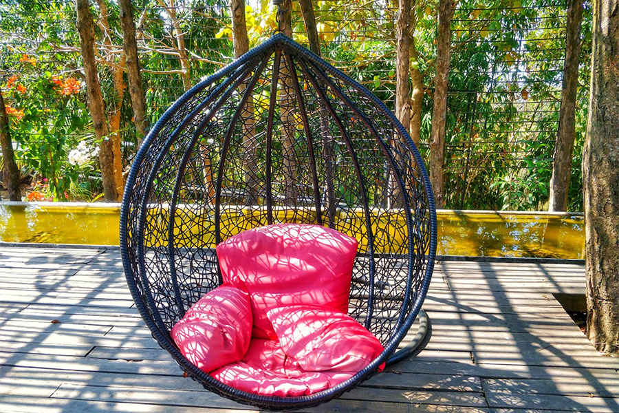 a hanging egg chair on a patio with pink pillows
