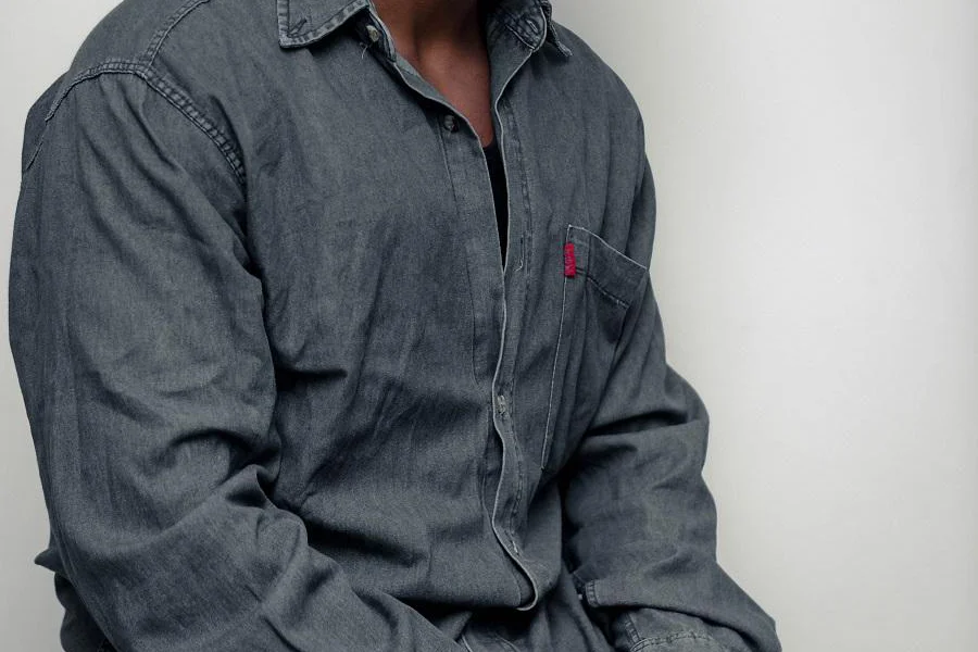 A man sitting while wearing a gray denim shirt