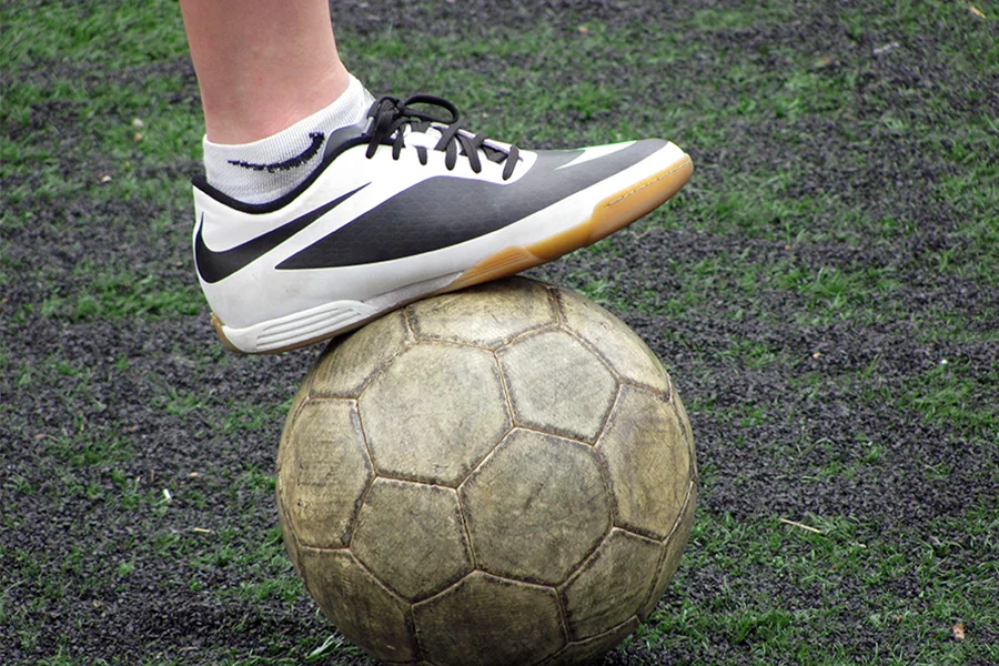 A soccer player placing a turf shoe on a soccer ball