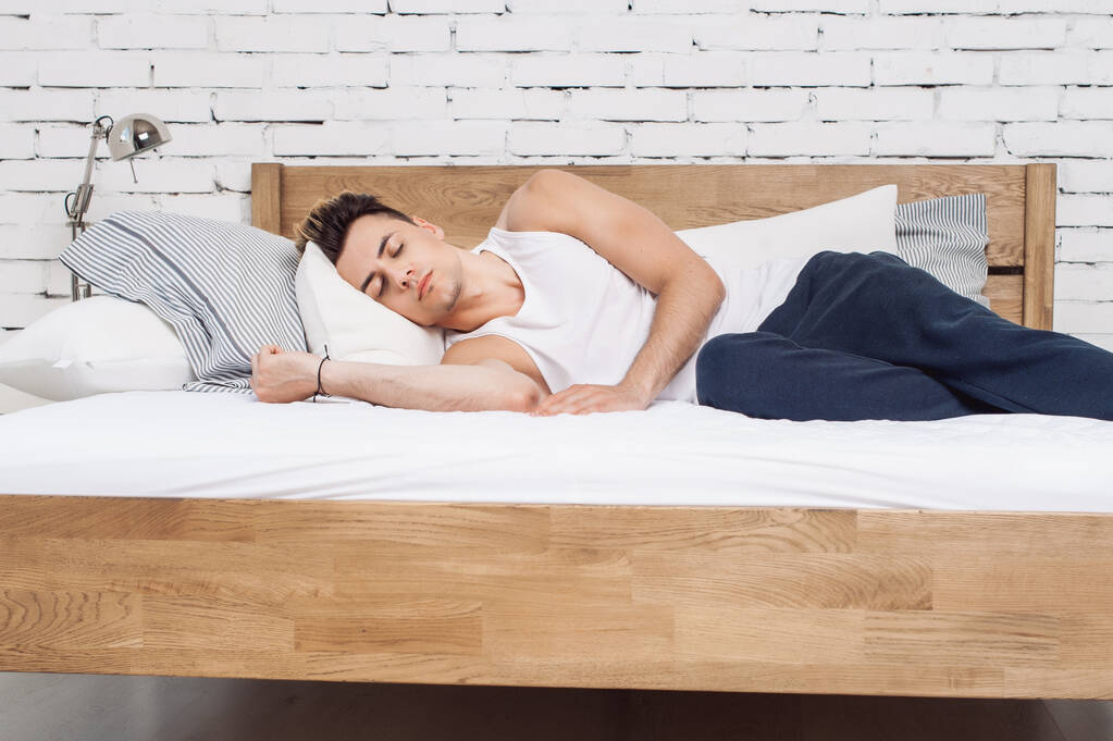 man lying sideways on a wooden framed bed with pillows