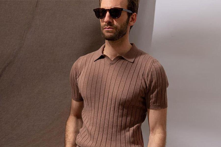 Male model in a brown knitted polo and white pants