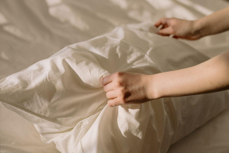 A person holding a white pillow over a bed