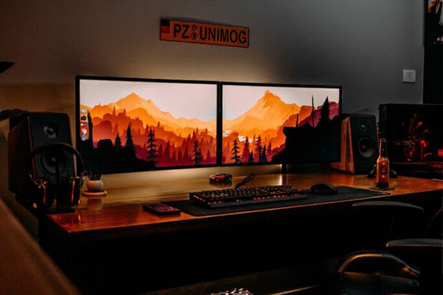 Two Monitors With Landscape Wallpapers In A Dark Room