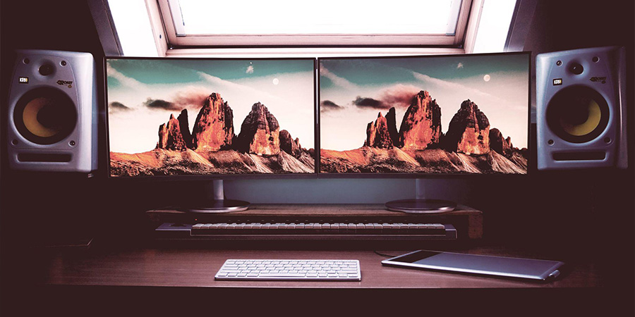 Two Monitors With Landscape Wallpapers In Front Of A Window