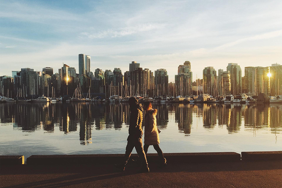 Two people walking along the water with the city in the background