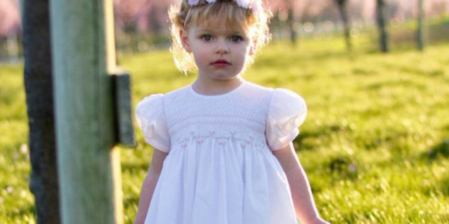 A young girl wearing a white smocked party dress