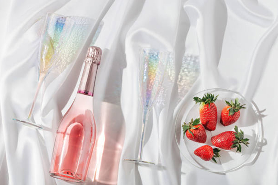 Champagne goblets on a bed with bottle and strawberries