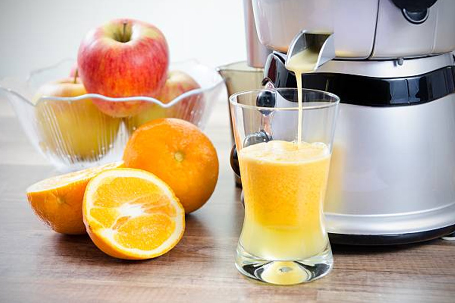 Juicing machine pouring out fresh orange and apple juice