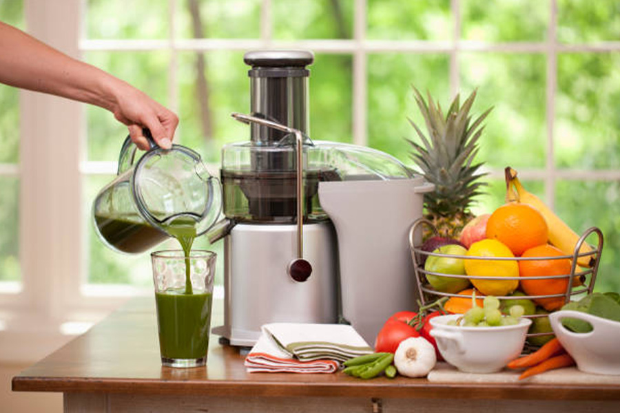 Large fruit juicer with glass of green smoothie being poured