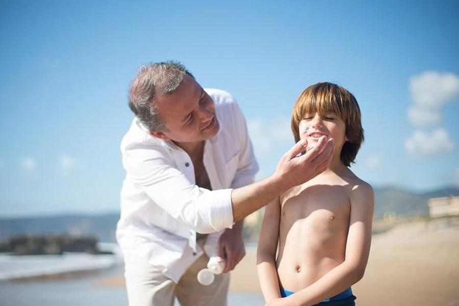 Man applying skincare sunscreen on a boy’s face on a sunny day