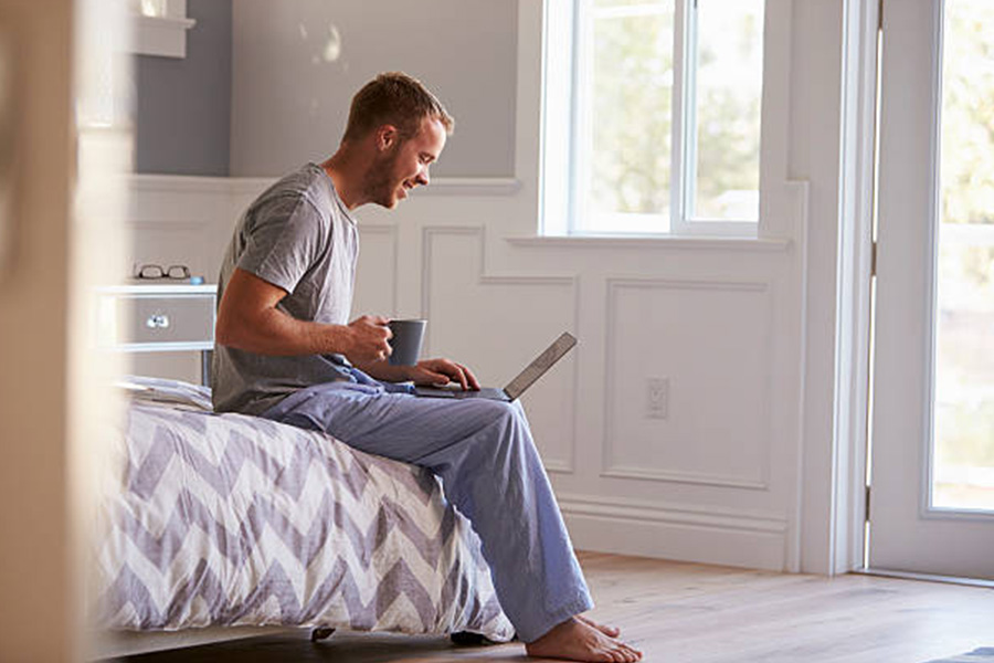 Man sitting on a bed in bamboo sleepwear with laptop