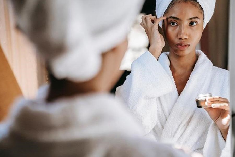 Woman in a bathrobe applying eye cream moisturizer on her face