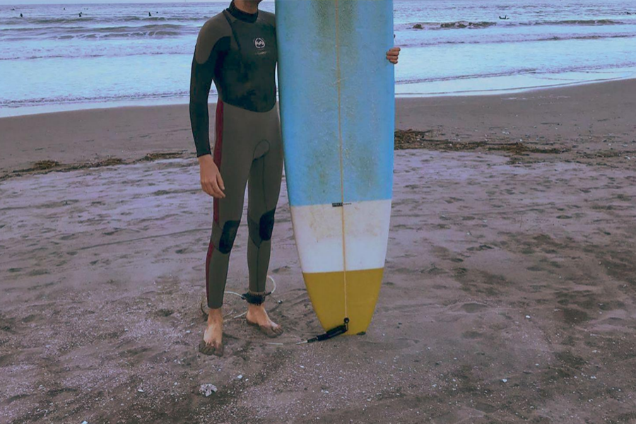 A man wearing a gray wetsuit holding a surfboard