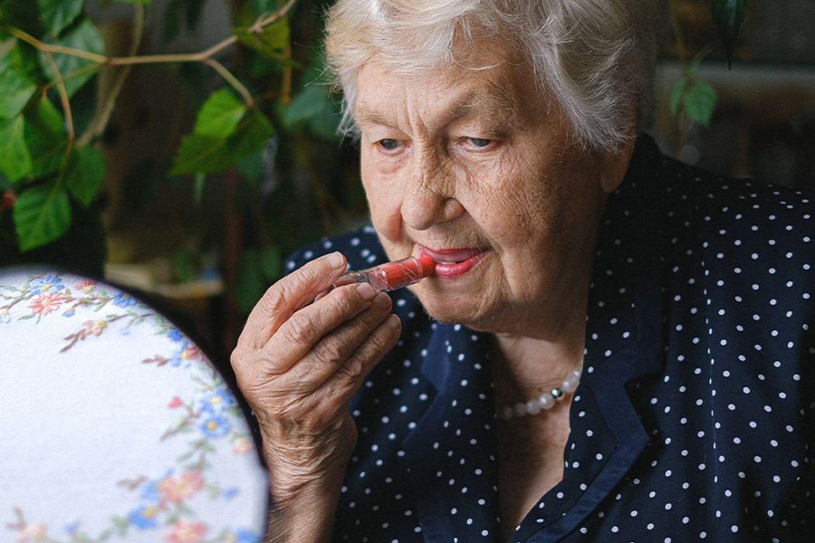 An elderly woman applying lipstick