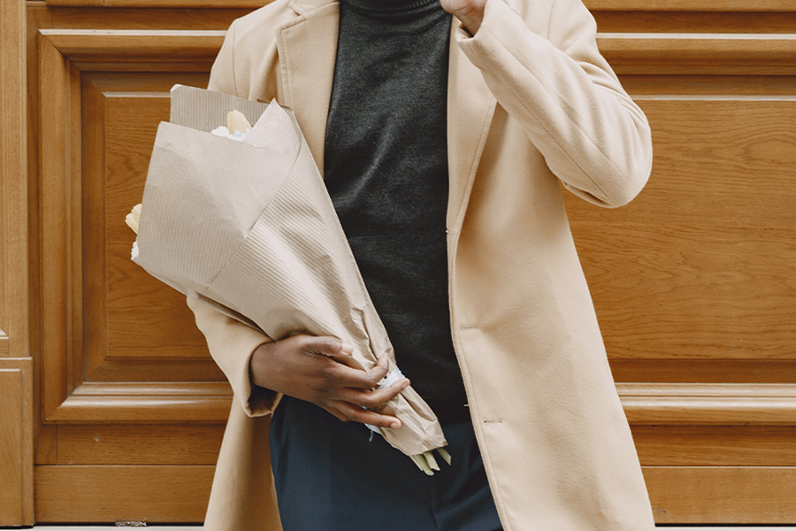 Man rocking cream duster jacket while holding flowers