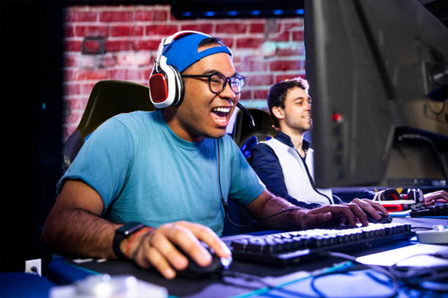 Two men at computers gaming while wearing wired headsets
