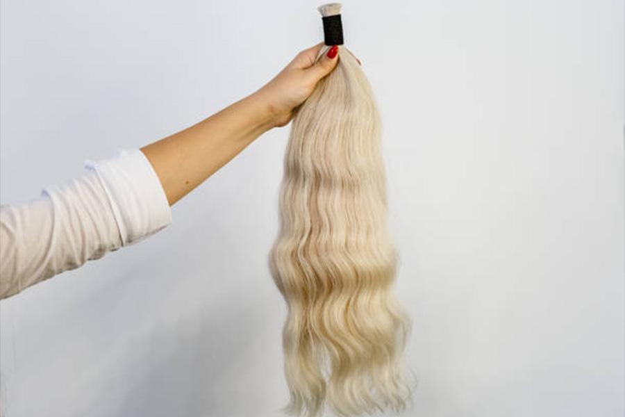 Woman holding a blonde hair extension against white wall