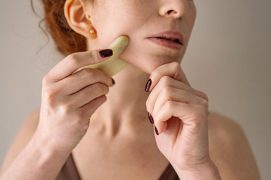 Woman performing Gua Sha skincare technique with stone tool