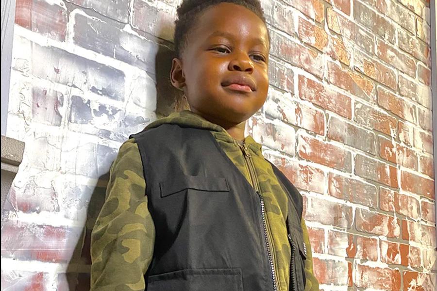 Young boy wearing a black utility vest over an army hoodie
