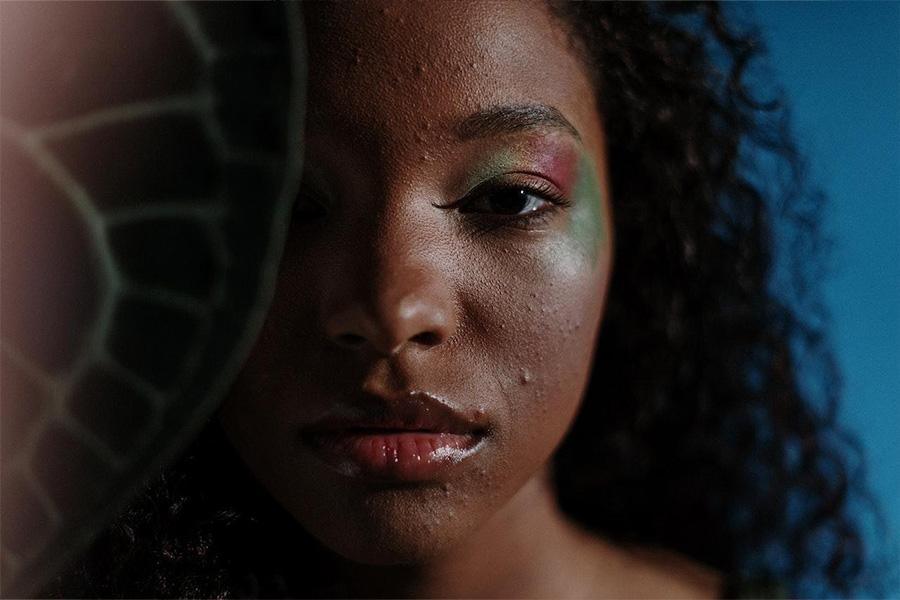 Black woman wearing pink and green makeup with imperfect skin