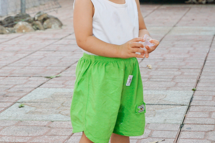 Boy holding plastic cup with green woven shorts