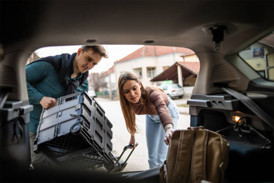 Couple packing suitcases into the trunk of a vehicle