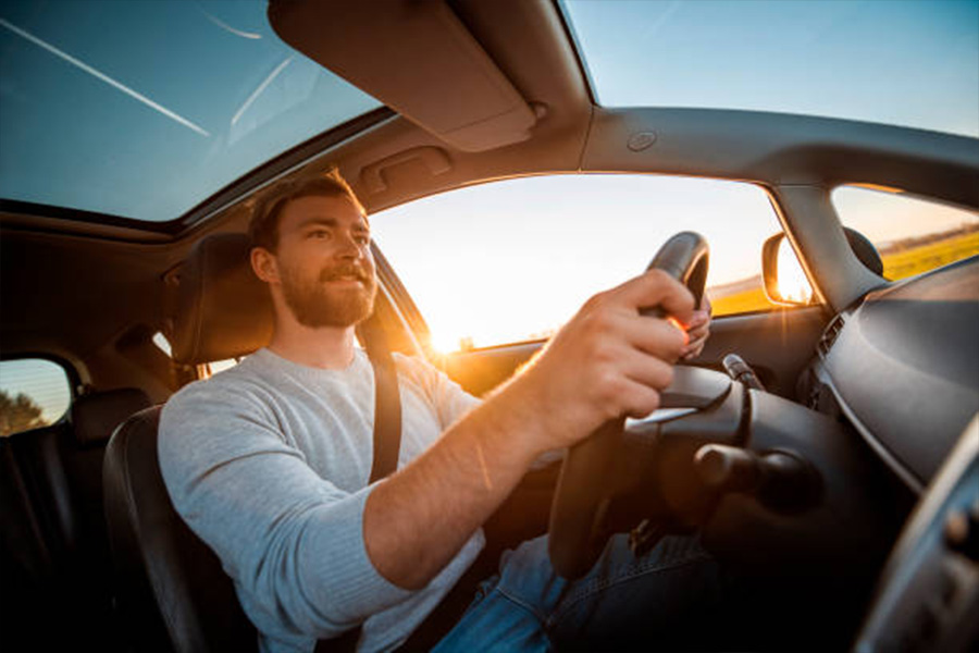 Man looking happy to be driving his car at sunset