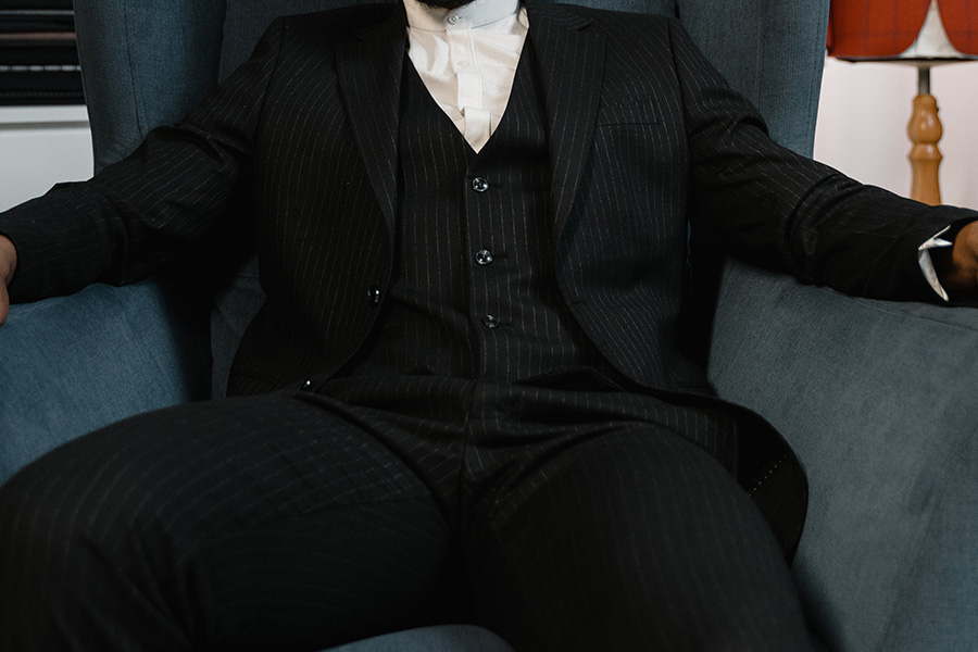 Man sitting on a chair in black pinstriped tailoring