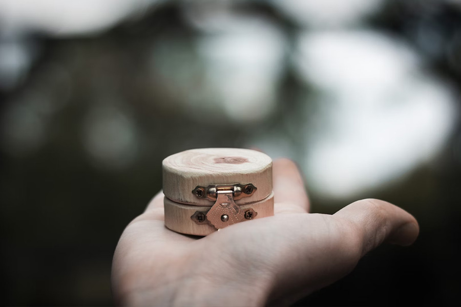 Tiny round wooden box with latch in palm of hand