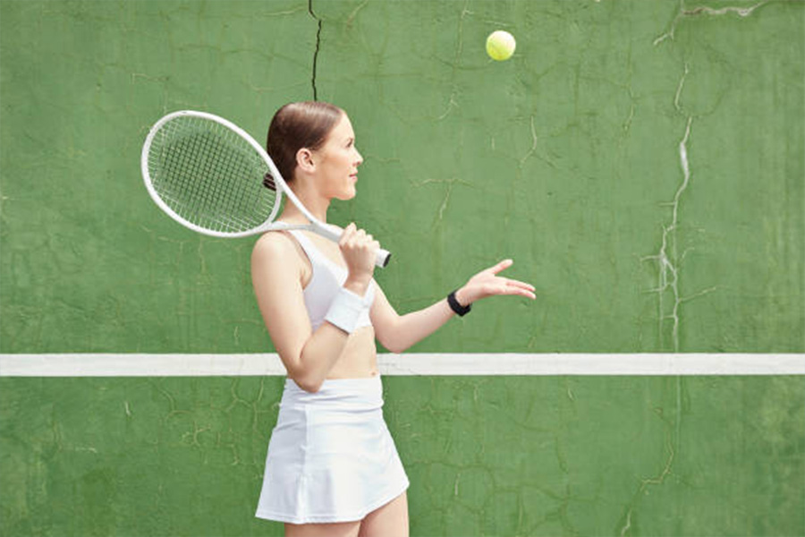 Woman in white tennis outfit throwing ball in the air