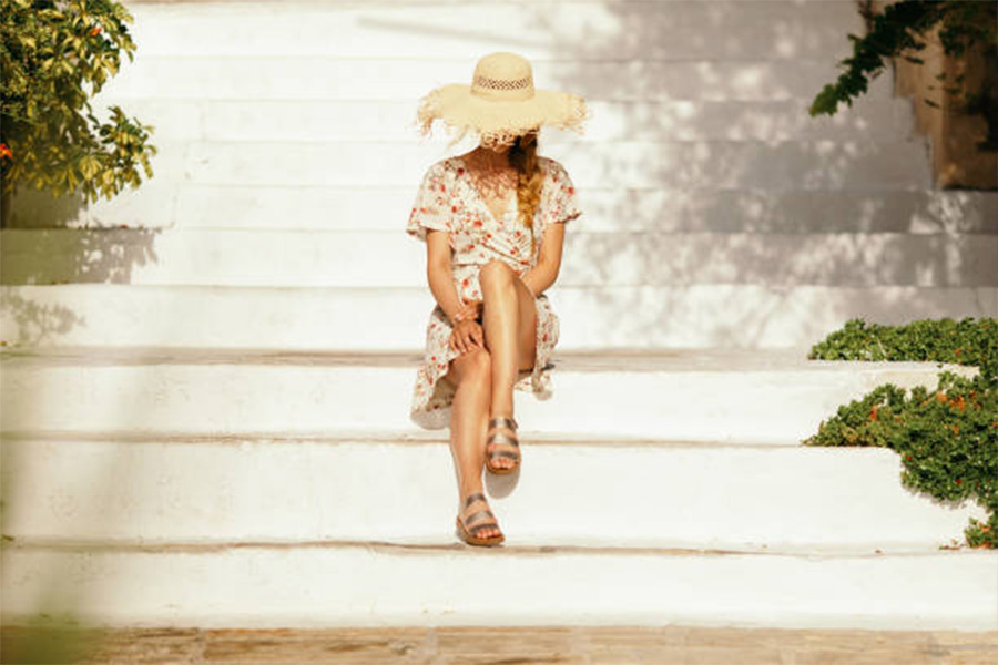 Woman sitting on white steps with straw hat and dress