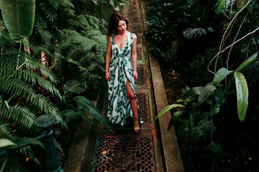 Woman wearing white and green tropical dress standing between plants