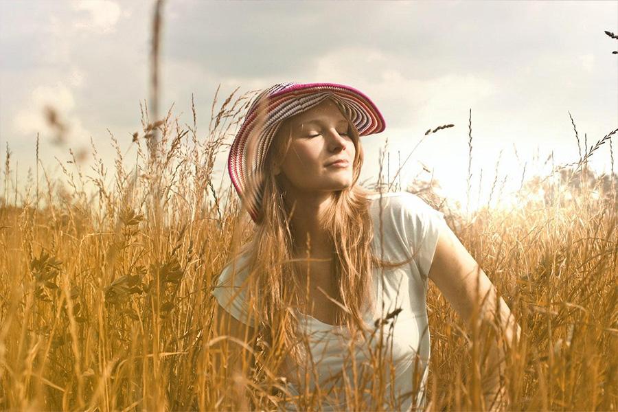 Woman wearing white top and red and white hat sitting in tall grass