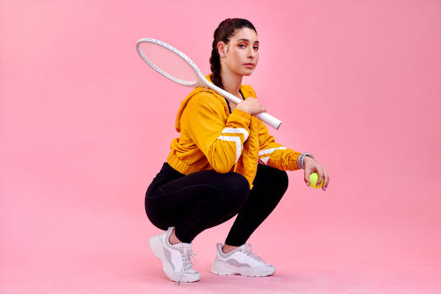 Woman with orange vintage windbreaker holding tennis racket and ball
