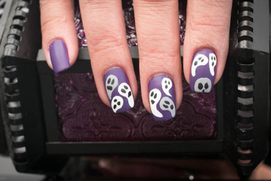 Woman’s nails painted purple with white ghosts on top