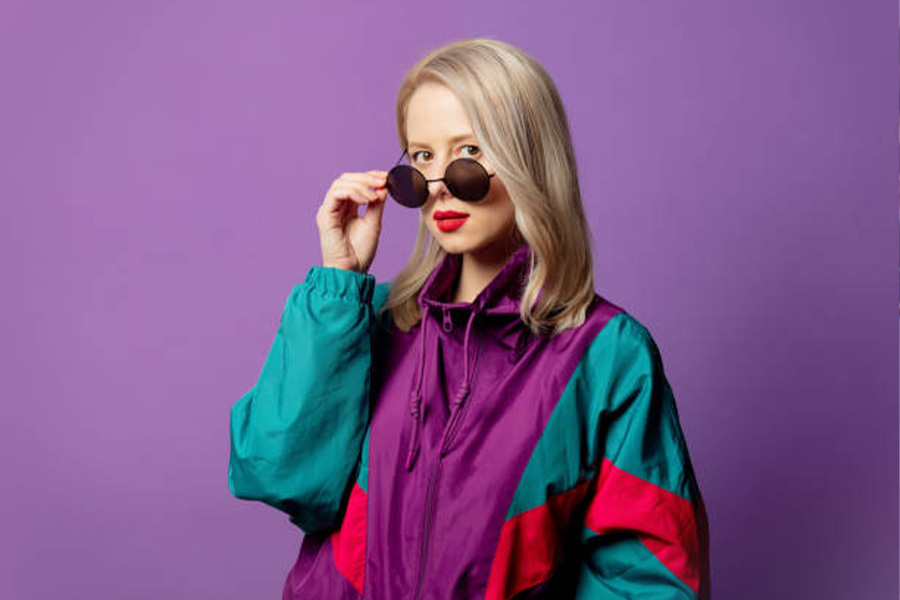 Blonde woman wearing a multi-color vintage windbreaker with sunglasses