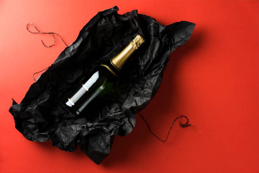 Bottle of wine sitting in black wrapping paper with ribbon