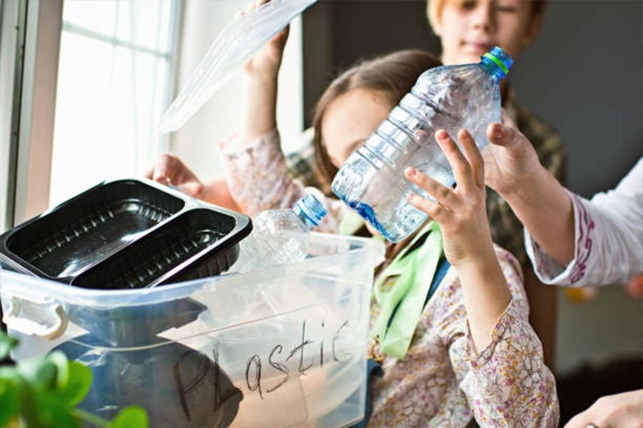Child placing a used water bottle in a plastic container
